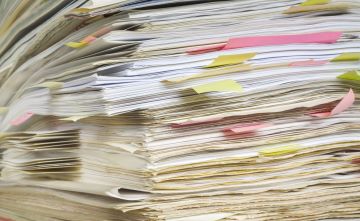 Closeup photo of a stack of papers, some with pink or yellow sticky notes